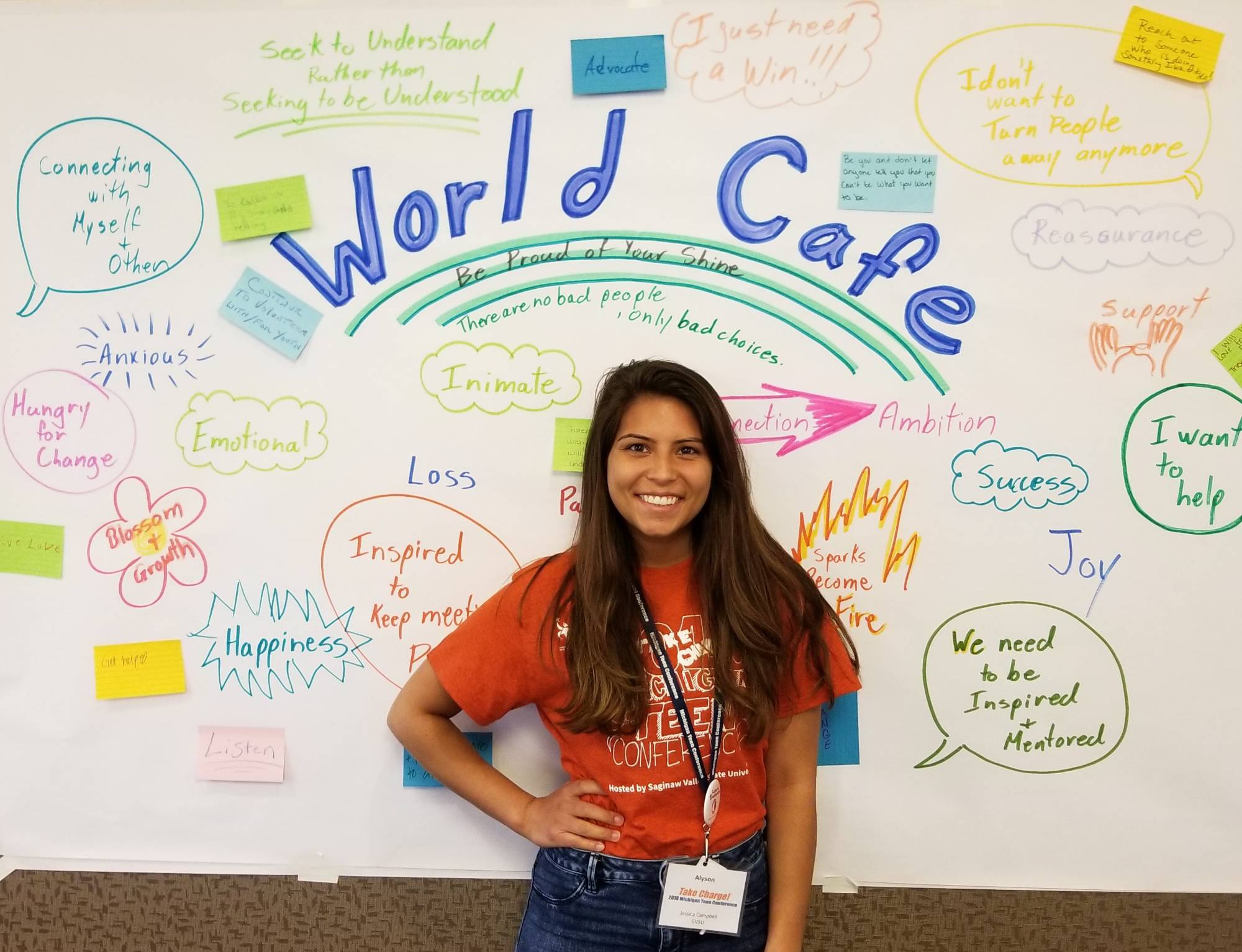 student smiling at camera in front of a world cafe poster